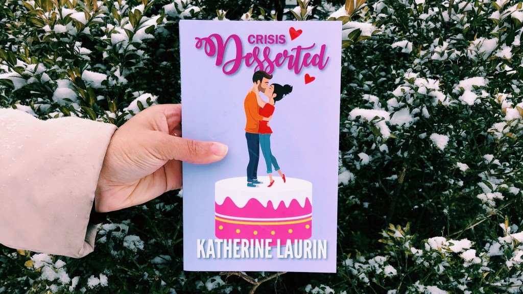 Independent Book review's Jaylynn Korrell holds the paperback of Crisis Desserted by Katherine Laurin in front of a snowy bush